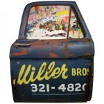 Front view of an artwork made with a 1965 Ford truck's door and torn posters.